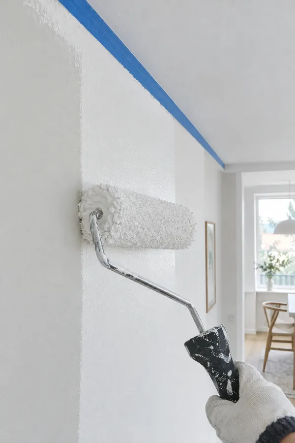 Paint roller applying white paint along a taped ceiling edge
